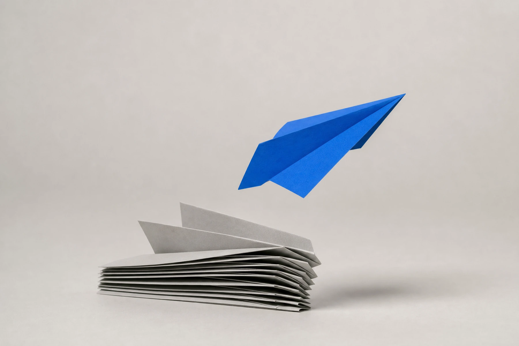 A blue paper plane lifting off a stack of grey ones